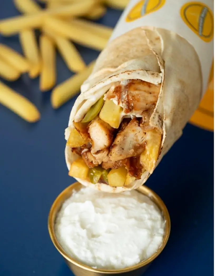 Sandwich shawarma poulet au-dessus d'un bol de sauce à l'ail